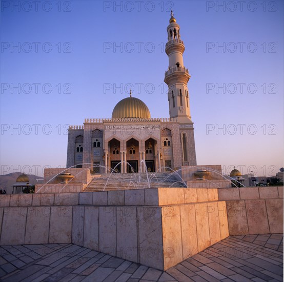 OMAN, Capital Area, Al Khuwair, Zawawi Mosque. Exterior seen at dusk with gold dome shining and fountain in the foreground.