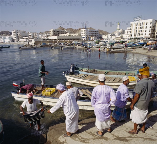 OMAN, Capital Area, Matrah, Fish Souk with locals unloading a catch at jetty. Boats and the waterfront in the background.