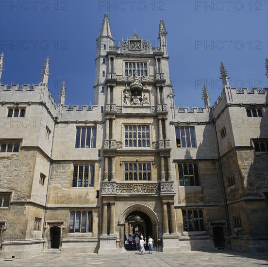 ENGLAND, Oxfordshire, Oxford, The Old Bodleian Library exterior facade with people walking through arched entrance to interior courtyard.
