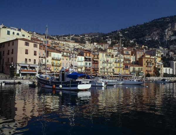 FRANCE, Provence Côte d’Azur, Alpes Maritimes, "Villefranche sur Mer, harbour with moored fishing boats and yachts, colourful quayside buildings and houses on hillside behind."