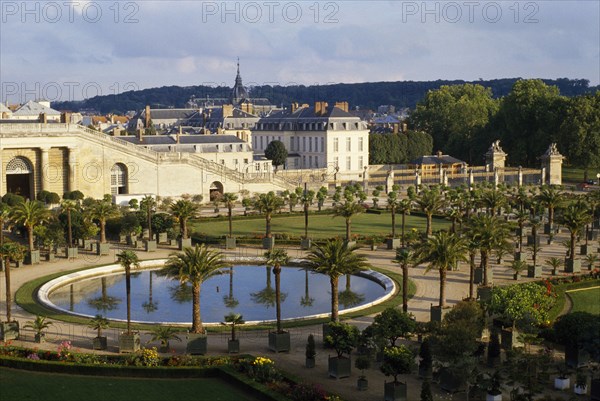 FRANCE, Ile de France, Versailles, General view over round pool surrounded by palms with the town behind