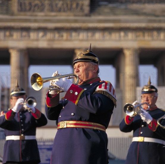 GERMANY, Berlin, Brass bandsmen in traditional uniform playing trumpet with the Brandenburg Gate behind