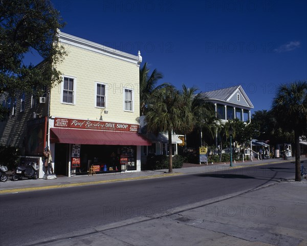 USA, Florida, Key West, View across an empty street lined with shopfronts including a Diving shop with palm trees and blue sky