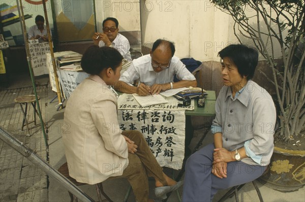 CHINA, Shaanxi, Xian, Professional letter writer with customers sitting at a desk outside the post office