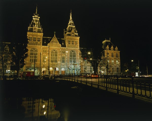 HOLLAND, North, Amsterdam, Rijksmuseum illuminated at night beyond a bridge over a canal reflected in the water