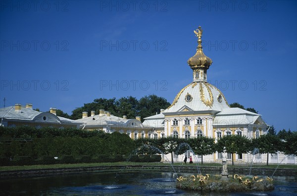 RUSSIA, St Petersburg, Petrodvorets, Yellow white and gold architecture seen across gardens and pond with central fountain.