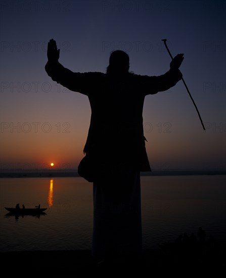 INDIA, Uttar Pradesh, Varanasi, Silhouette at sunset of a Holy Man on the banks of the River Ganges with his arms outstretched