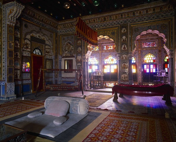 INDIA, Rajasthan, Jodhpur, Meherangarh Fort.  Interior of the bedroom of the Maharajah with light coming through stained glass window.