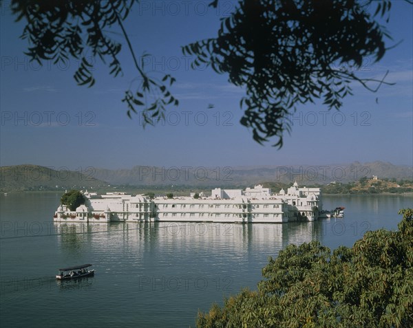 INDIA, Rajasthan, Udaipur, The Lake Palace in the middle of the lake with a covered boat making its way across the water
