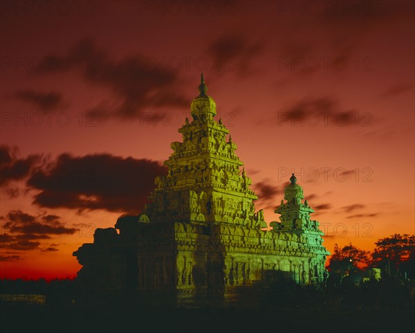 INDIA, Tamil Nadu, Mahabalipuram, Shore Temple.  Tower floodlit at dusk with dramatic orange sky and clouds