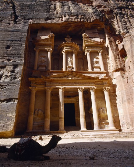 JORDAN, Petra, The Treasury.  Porticoed entrance carved in pink rock with camel lying down in foreground.