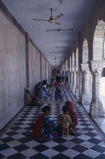 INDIA, Delhi, "Sikh pilgrims sitting on long, colonnaded temple passage-way with black and white chequered pattern floor."