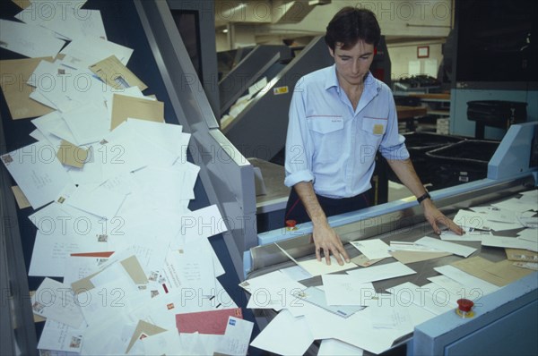 ENGLAND, East Sussex, Brighton, Mail sorting office.  Male worker sorting through letters on conveyor belt to culler.
