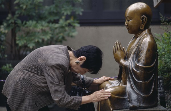 JAPAN, Religion, Woman praying before a seated Buddha