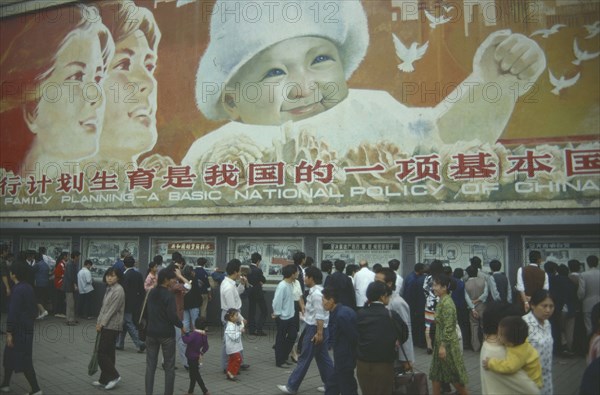 CHINA, Sichuan Province, Chengdu, Busy street with pedestrains walking past family planning poster displayed overhead.