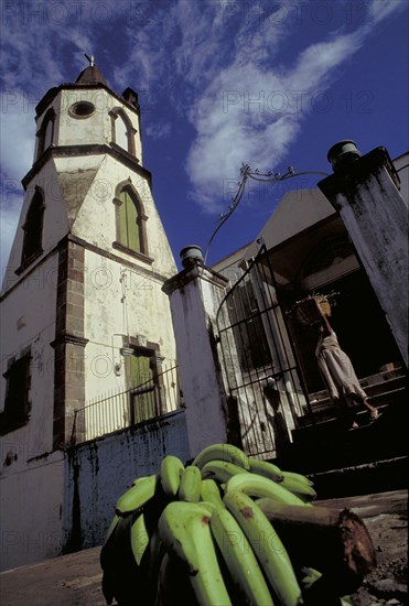 WEST INDIES, Dominica, Roseau, The Methodist Church with Harvest Festival Offering of bananas on the pavement as woman leaves the church
