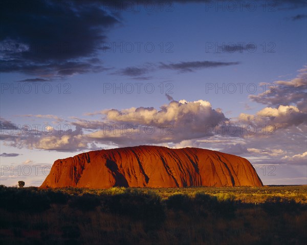 AUSTRALIA, Northern Territory, Uluru, Ayers Rock.  Giant red rock formation at dusk overshadowed by storm clouds