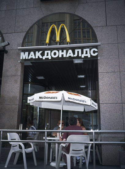 RUSSIA, Moscow, McDonalds Restaurant with people sitting at table and chairs with umbrella outside entrance with restaurant sign in Russian
