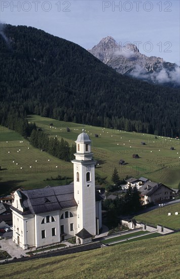 ITALY, Trentino, The Dolomites, The village church of Sesto in the Val di Sesto set below forested hills and snow capped mountains