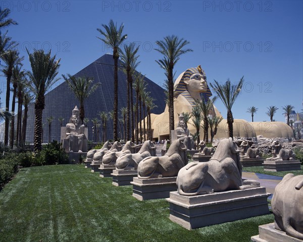 USA, Nevada, Las Vegas, Luxor Hotel and Casino Pyramid shaped building with Sphinx and row of stone rams on lawns beside a palm lined avenue