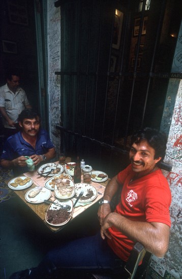 CUBA, Havana, "Bodequita del Medio Bar with two men sitting at a table covered in semi finnished plates of rice, beans and meat"