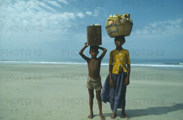 INDIA, Goa, Colva, Boy and girl from Karnataka on beach carrying fruit and drinks to sell to tourists