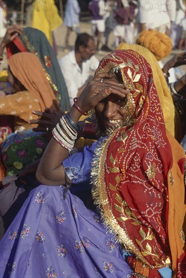 INDIA, Rajasthan, Pushkar, Seated smiling Rajasthani woman in colourful sari looking over her shoulder towards camera.
