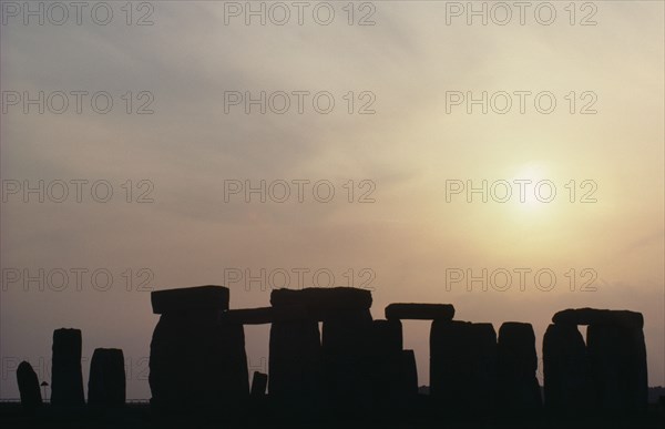 ENGLAND, Wiltshire, Stonehenge, Standing stones on Salisbury Plain silhouetted at sunset with a yellow sky