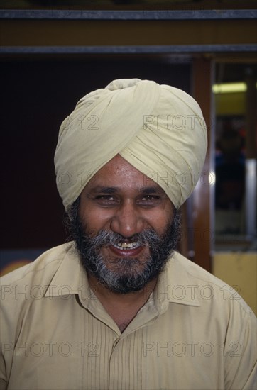 ENGLAND, London, Head and shoulders portrait of a Sikh man smiling wearing a beige turban