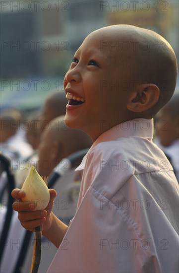 THAILAND, North, Chiang Mai, Laughing novice monk dressed in white holding a lotus flower during a mass ordination ceremony