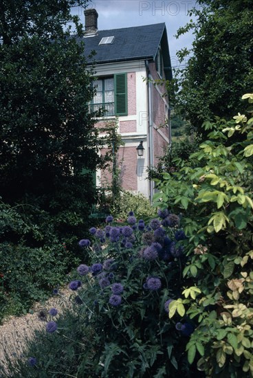 FRANCE, Normandy, Eure , Giverny. Claude Monet’s house with shuttered windows seen through garden foliage.