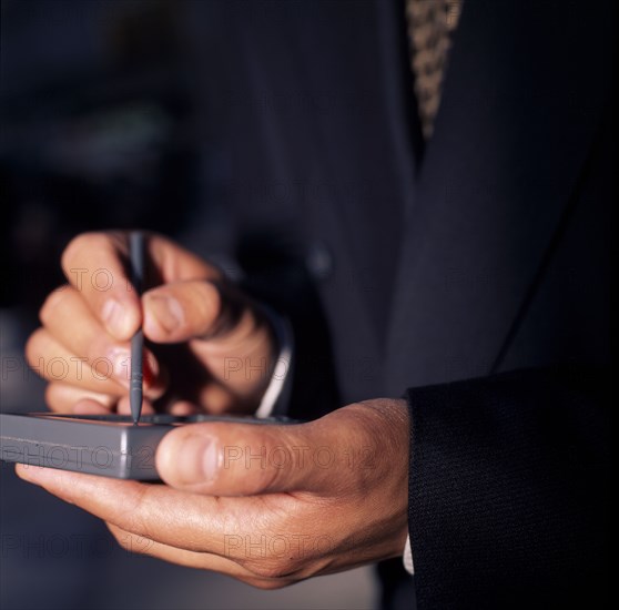 USA, New York, Detail of businessman’s hands using PDA palm held personal organiser.