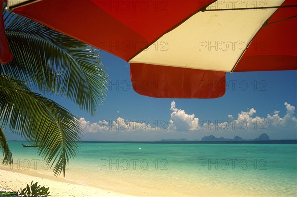 THAILAND, Trang Province, Koh Hai, Koh Kraddan in the distance across clear calm blue sea seen from beneath an umbrella on the beach