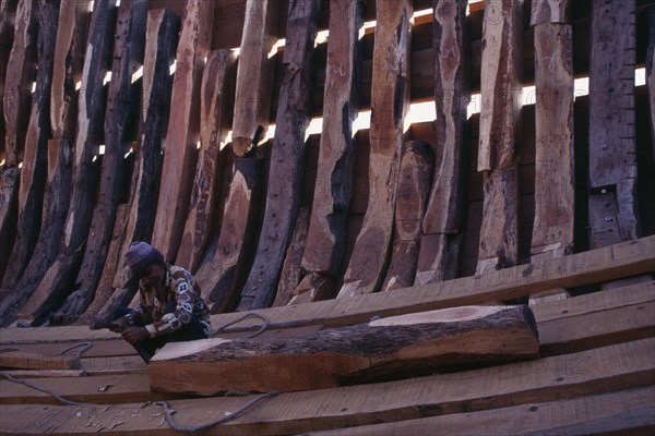 INDIA, Gujarat, Veraval, Shipbuilding.  Man working on interior shell of boat.