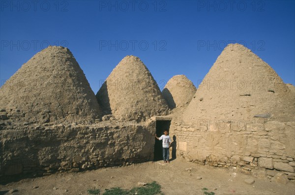 TURKEY, Urfa, Harran  , Beehive mud houses with boy standing at doorway