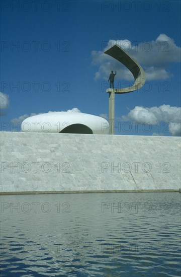 BRAZIL, Federal District, Brasilia, Kubitschek Memorial with large sculpture holding a statue seen over surrounding pool
