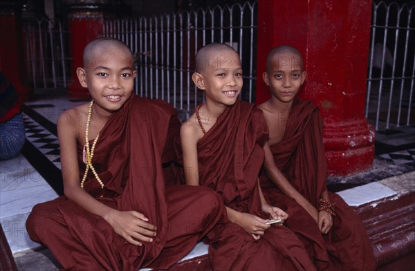 MYANMAR, Yangon, Shwedagon Pagoda, Three young monks sitting on the floor at the front of the temple