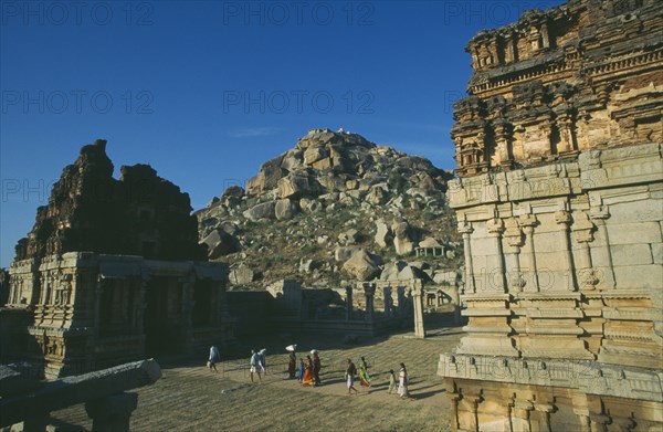 INDIA, Karnataka, Hampi, Achyutaraya Temple with Matanga Hill in the background and people walking between buildings in the foreground.