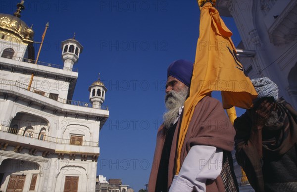 INDIA, Punjab, Amritsar, Golden Temple with a pilgrim flag bearer carrying the Sikh orange flag or Nishan Sahib.