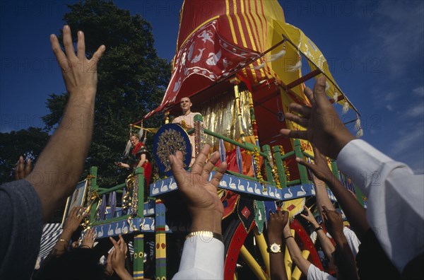 RELIGION, Hare Krishna, View over the reaching hands of a crowd toward brightly decorated cart with two people standing on the top during a festival