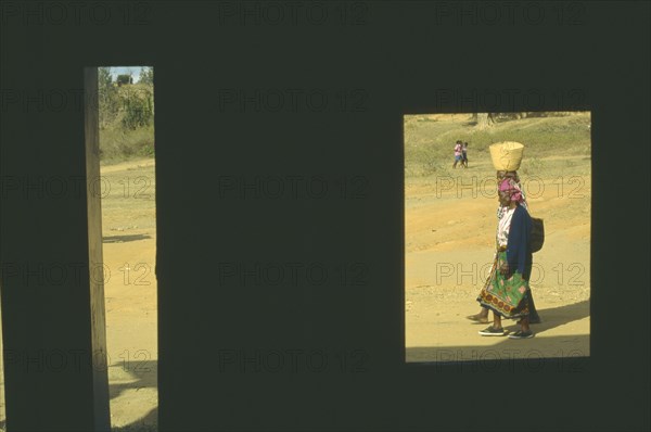 KENYA, Voi, Women carrying baskets framed by window of building in deep shadow.