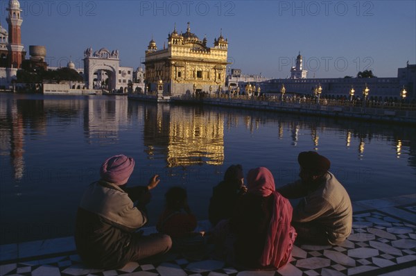 INDIA, Punjab, Amritsar, Golden Temple.  General view with pilgrim group sitting beside sacred pool in the foreground.