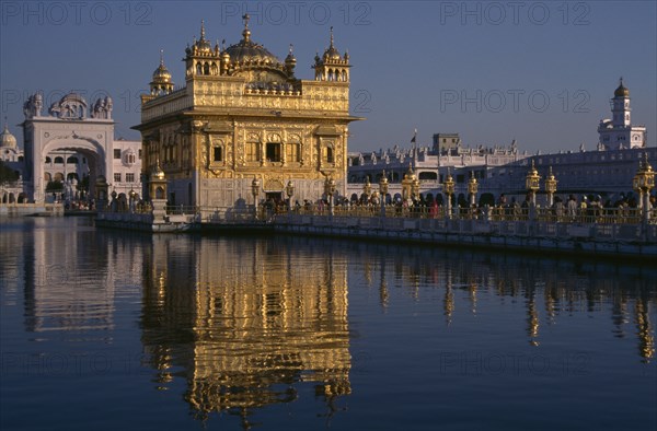 INDIA, Punjab, Amritsar, Golden Temple with pilgrims and visitors on causeway or the Guru’s Bridge leading to temple reflected in rippled surface of pool.