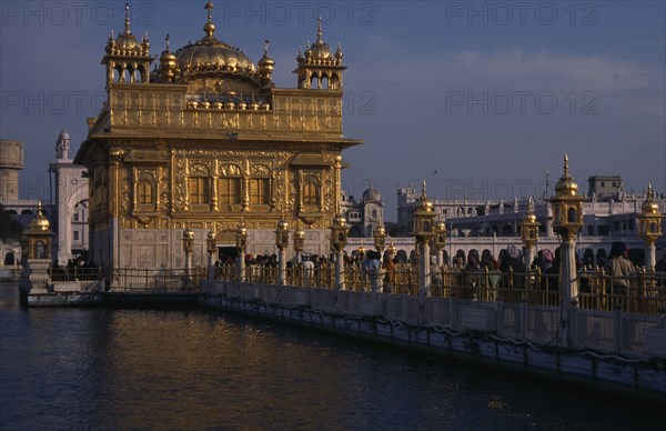 INDIA, Punjab, Amritsar, Golden Temple. Pilgrims and visitors on causeway known as the Guru’s Bridge approaching temple.