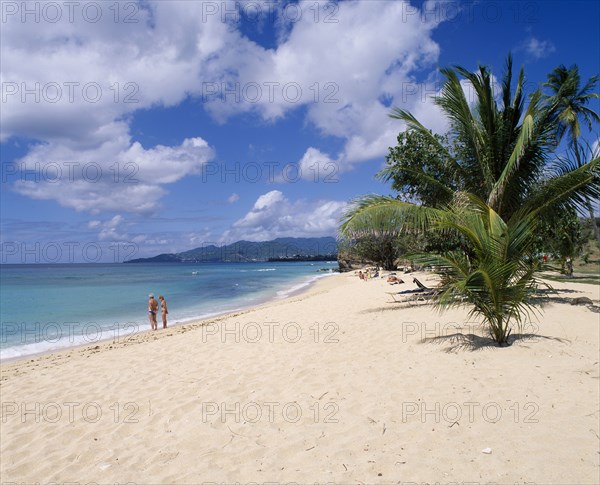 WEST INDIES, Grenada, Magazine Beach, View along quiet sandy beach with a couple standing at the waters edge