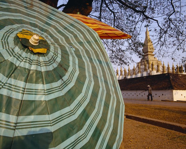 LAOS, Vientiane, Pha That Luang Sacred Stupa with large green striped umbrella in foreground.