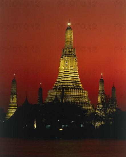 THAILAND, Bangkok, Wat Arun Temple Of The Dawn illuminated at sunset with orange sky and river in foreground