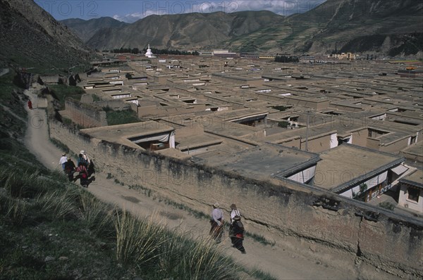 CHINA, Gansu, Xiahe , View over the rooftops of the Labrang Monastery with people walking a path running alongside the exterior wall