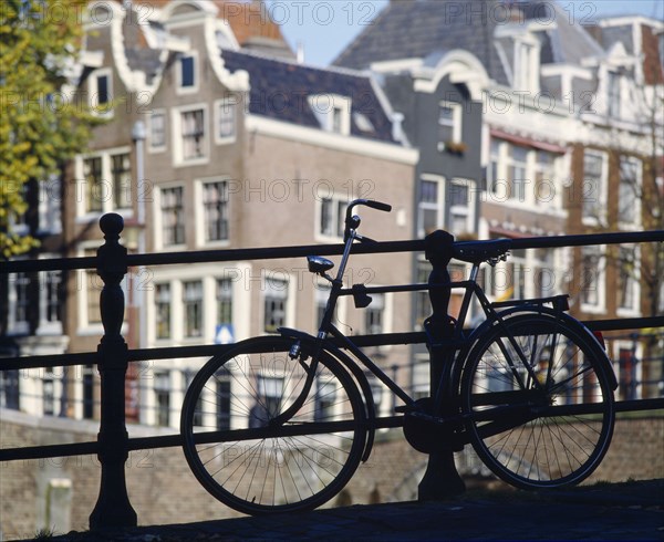 HOLLAND, North, Amsterdam, Bike parked against railings with traditional architecture behind.