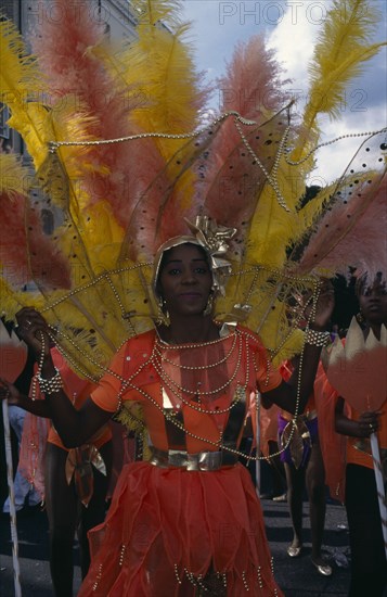 ENGLAND, London, Notting Hill Carnival. Woman in orange costume with orange and yellow feathers and gold head-dress.